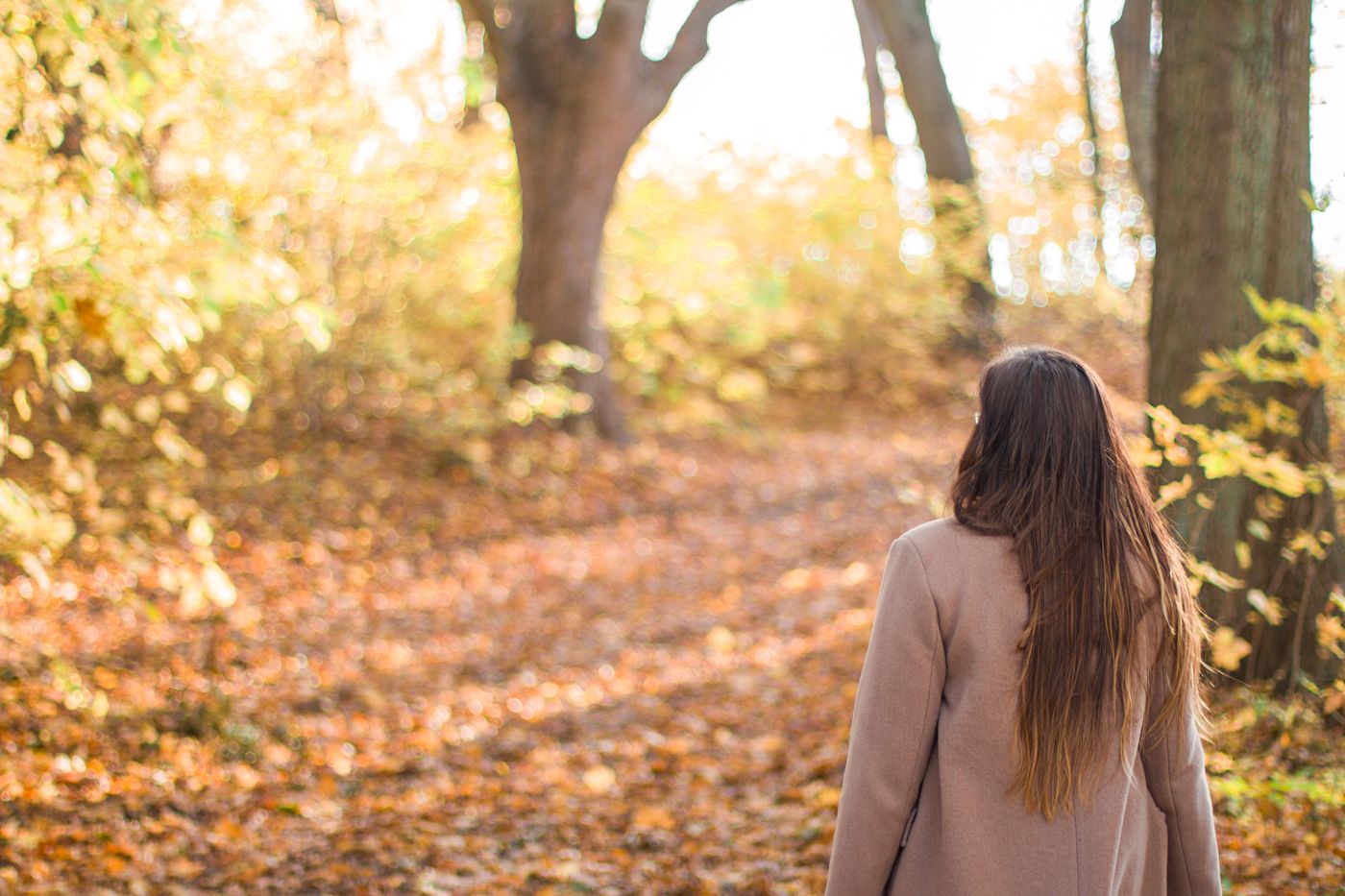 Une femme marche sur un chemin de forêt baigné de lumière
